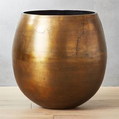 a large metal vase sitting on top of a wooden table next to a white wall