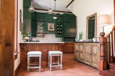 two stools in the middle of a kitchen with dark green cabinets and white counter tops