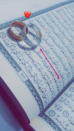 two wedding rings sitting on top of an open book with arabic writing in the background