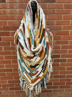 a multicolored crocheted shawl hanging on the side of a brick wall