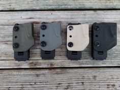 four different colored holsters are lined up on a wooden surface, one is black and the other is white