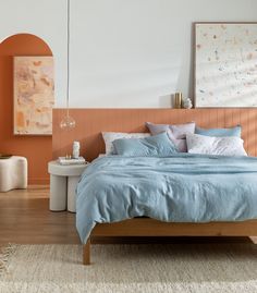 a bed with blue linens and pillows in a white room next to an orange wall