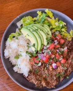 a bowl filled with meat, rice and avocado on top of a wooden table