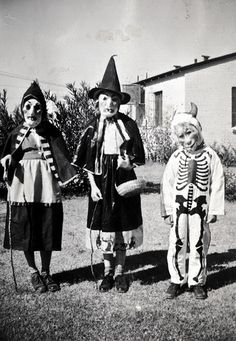 three children dressed up in halloween costumes standing on the grass with one holding a broom