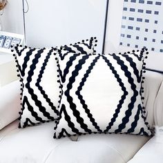 two black and white pillows sitting on top of a white couch next to a book