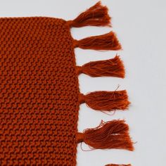 an orange knitted scarf with tassels laying on top of it, against a white background