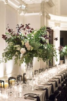 a long table is set with wine glasses and vases filled with flowers on it