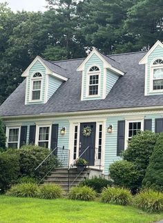 a blue house with black shutters on the front and side windows, surrounded by greenery