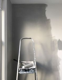 a ladder is in front of a gray wall with white paint