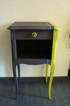 a small wooden table with a yellow drawer on the top and green legs next to a potted plant