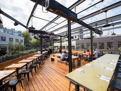 people are sitting at tables in an outdoor dining area with wood floors and metal roofing