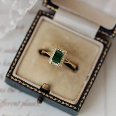 an engagement ring with a green stone sits in a box on top of a piece of paper