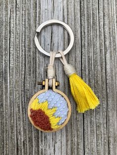 a keychain with a sunflower embroidered on it, hanging from a wooden background