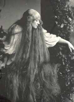 an old black and white photo of a woman with long hair standing next to a plant