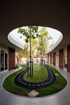 an empty tennis court in the middle of a building with grass and trees on both sides