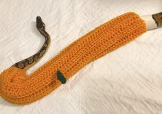 an orange crocheted umbrella with a snake on the top and bottom, sitting on a white sheet