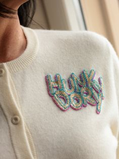 a woman wearing a white sweater with colorful sequins on the letters ugly god