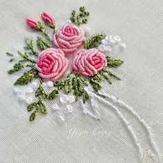 pink roses and green leaves on white linen with beadings in the center, sitting on a black surface