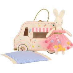 a stuffed rabbit in a pink tutu next to a toy food truck and pillow