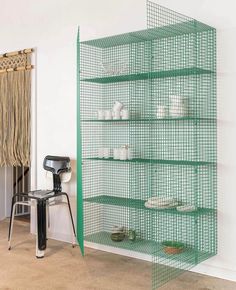 a green shelf filled with dishes next to a chair