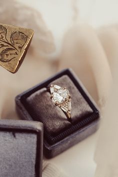 an engagement ring sits in a box next to two other wedding rings on top of each other