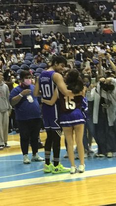 two women in purple uniforms hugging each other on a basketball court while people watch from the bleachers