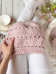 a woman is holding onto a pink crocheted hat