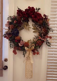 a wreath hanging on the front door with flowers and leaves around it, along with other decorations