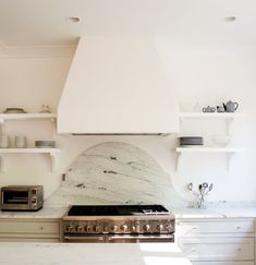 a stove top oven sitting inside of a kitchen next to white cabinets and shelves filled with dishes