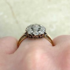 a close up of a person's hand holding an old fashioned diamond engagement ring