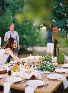 a group of people standing around a wooden table covered in food