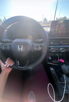 a woman driving a car with her hand on the steering wheel while holding onto an electronic device