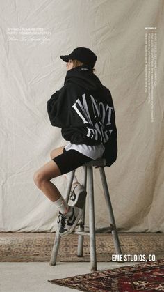 a person sitting on a stool wearing a black hoodie and white shorts with the words not me printed on it