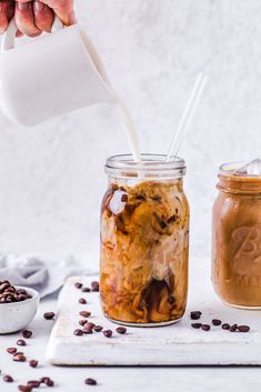 a person pouring milk into a mason jar filled with coffee beans and topped with chocolate chips