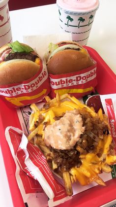 two cheeseburgers and fries on a tray with paper wrappers next to drinks