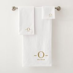 two white towels hanging on a towel rack with the letter o in gold foiled lettering