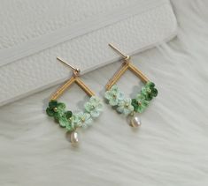 two pairs of earrings with green flowers and pearls on top of white furnishing