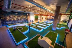 an indoor miniature golf course is lit up with blue and green lights on the walls