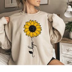 Item details Handmade Hope Sunflower Sweatshirt, Sunflower Gift Sweatshirt, Floral Sunflower Sweatshirt, Woman Fall Sweatshirt, Garden Sweatshirt, Autumn Sweater. We use first quality GILDAN brand HOW DO I KNOW WHAT SIZE FITS ME BEST Please see the size chart in our photos. Perfect for all family members. The adult shirts are now a unisex T-shirt so order accordingly. Most men order their normal size and women normally go down one size. Customers say that the youth and toddler shirts are true to size yet you have a size chart you can view in our photos.You can reach out to request a shirt in infant size should that be something you are interested in. BEST WAY TO ORDER 1. Select the size 2. Select the primary color 3. Click "add to cart" and then return to the listing for each family member Yellow Long Sleeve Tops With Sunflower Print, Yellow Long Sleeve Top With Sunflower Print, Spring Long Sleeve Top With Sunflower Print, Spring Long Sleeve Sunflower Print Top, Long Sleeve Sunflower Print Tops For Spring, Fall Crew Neck Top With Sunflower Print, White Crew Neck Top With Sunflower Design, Relaxed Fit Crew Neck Top With Sunflower Design, Relaxed Fit Sunflower Crew Neck Top