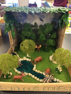 an open cardboard box filled with fake animals and trees in it's display area