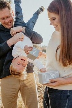 a man and woman holding a baby in the air with two other people around them