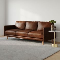 a brown leather couch sitting on top of a wooden floor next to a white wall