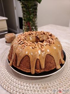 a bundt cake with frosting and nuts on top sitting on a plate next to a vase