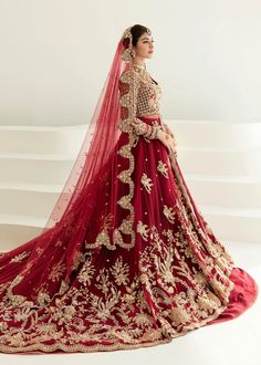 a woman in a red and gold bridal gown standing on a white surface with her arms behind her back