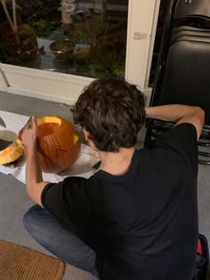 a man carving a pumpkin on the floor in front of a window with his hands