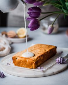 a piece of cake sitting on top of a white plate next to purple tulips