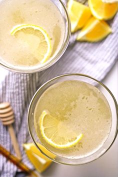 two glasses filled with lemonade sitting on top of a table next to sliced oranges