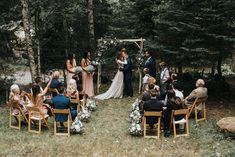 a wedding ceremony in the woods with people sitting on chairs and looking at each other