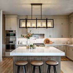 a kitchen island with stools in front of it and lights hanging from the ceiling