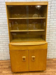 an old wooden cabinet with glass doors on the top and bottom shelves, in front of a brick wall